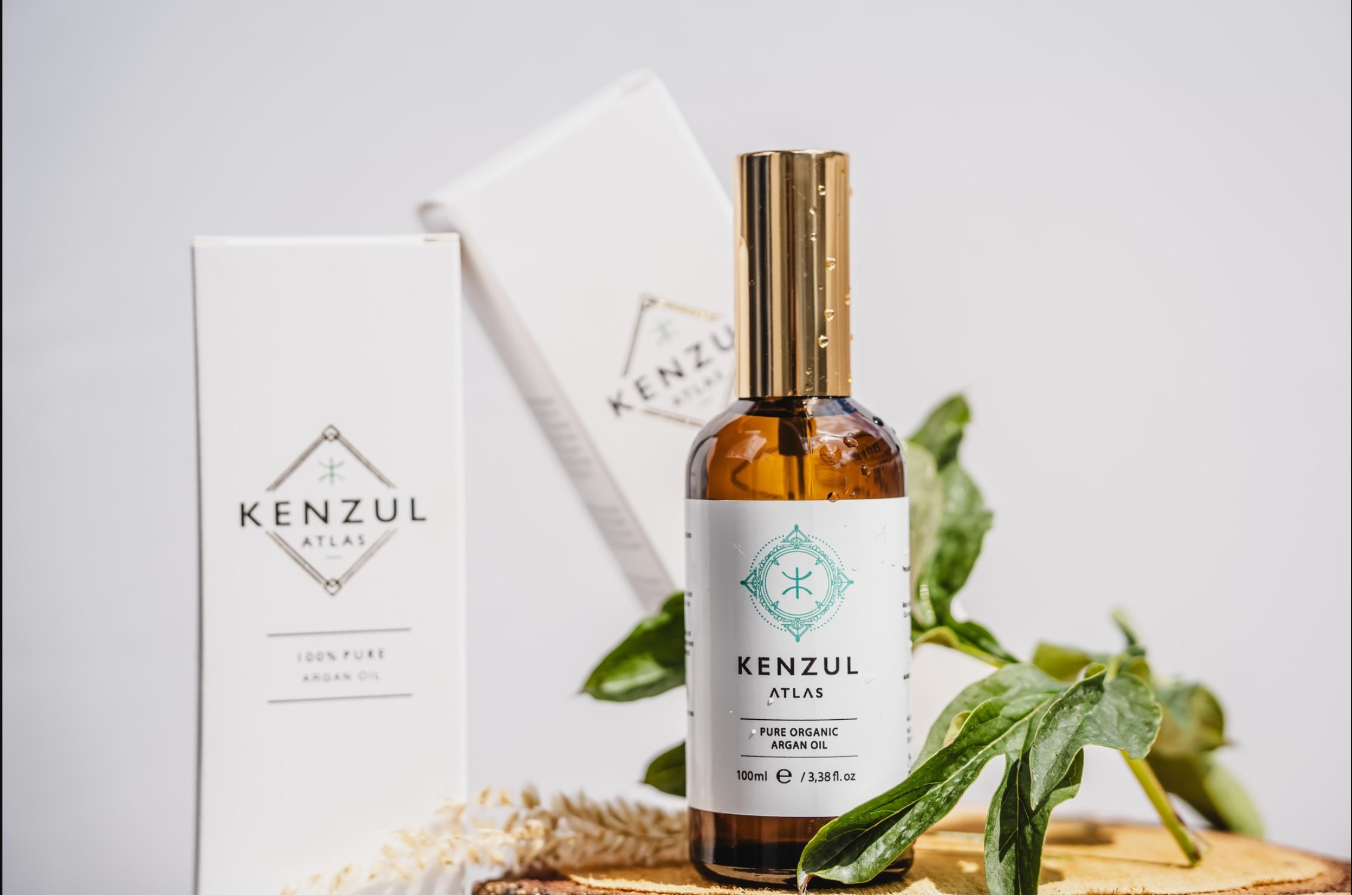 Kenzul Atlas Argan Oil 100ml amber glass bottle beside its box, with fresh argan leaves